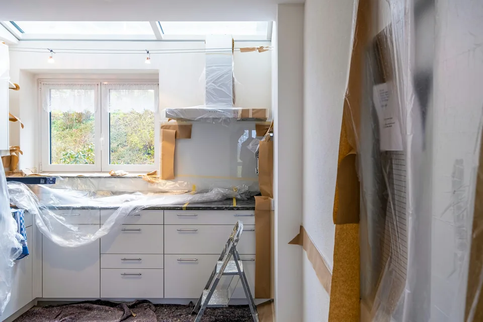 A kitchen during a renovation, with plastic sheeting over the range hood and the counters, paper taped to the walls and a stepladder on the covered floor