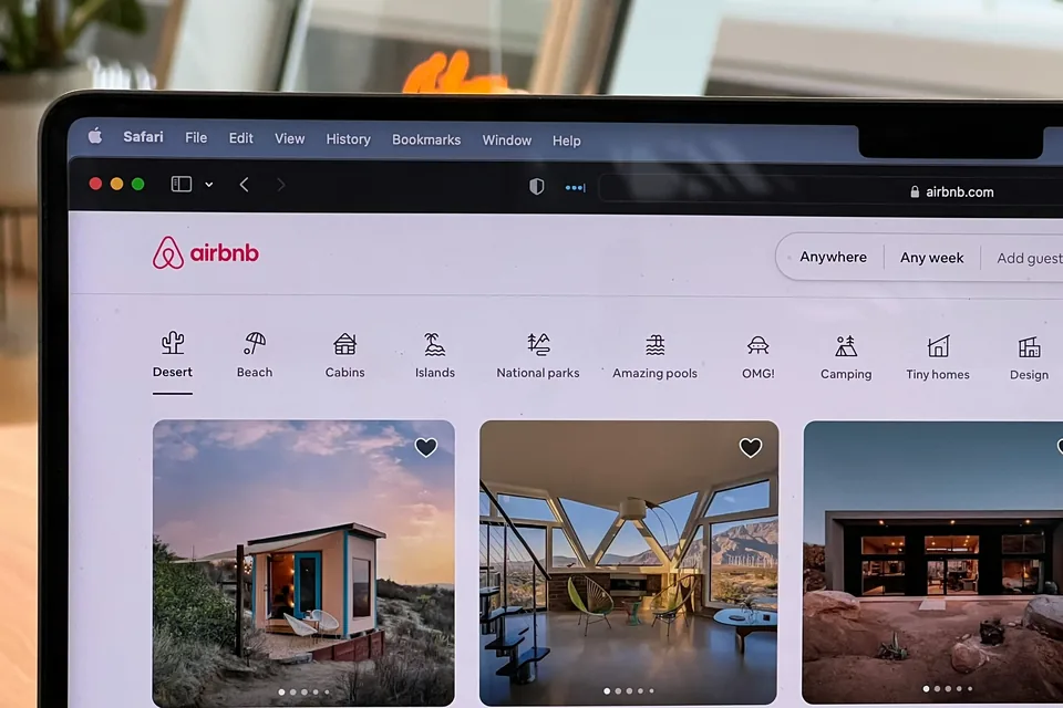 A laptop screen showing the Airbnb home page, with a row of photos of short-term rental listings