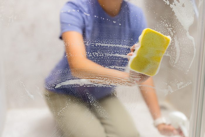 A cleaner wiping down shower glass in a condo bathroom
