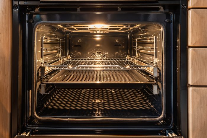 The inside of a spotless oven with the door open and the light on