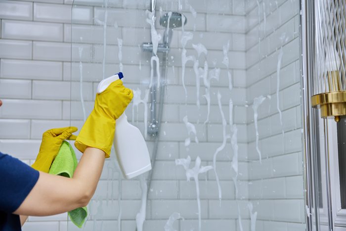 A cleaner spraying and wiping tiled shower walls during a deep clean