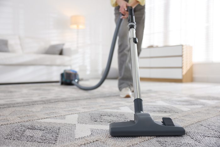 A cleaner vacuuming the rug in a living room
