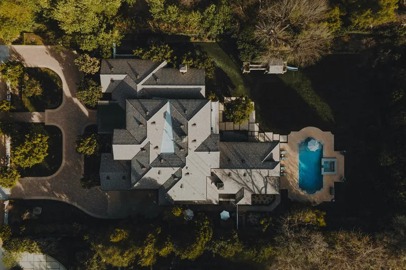 Aerial view of a large home surrounded by trees and a pool
