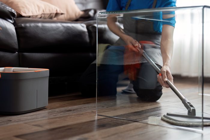 A cleaner mopping a hardwood floor beside a cleaning caddy