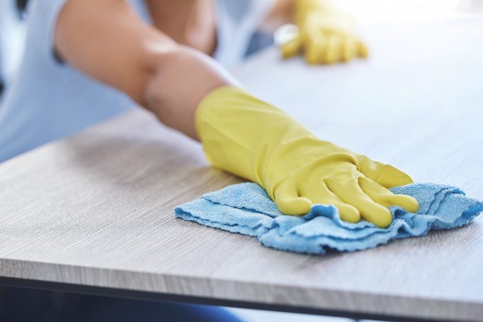 A gloved hand wiping down a wooden table with a microfibre cloth