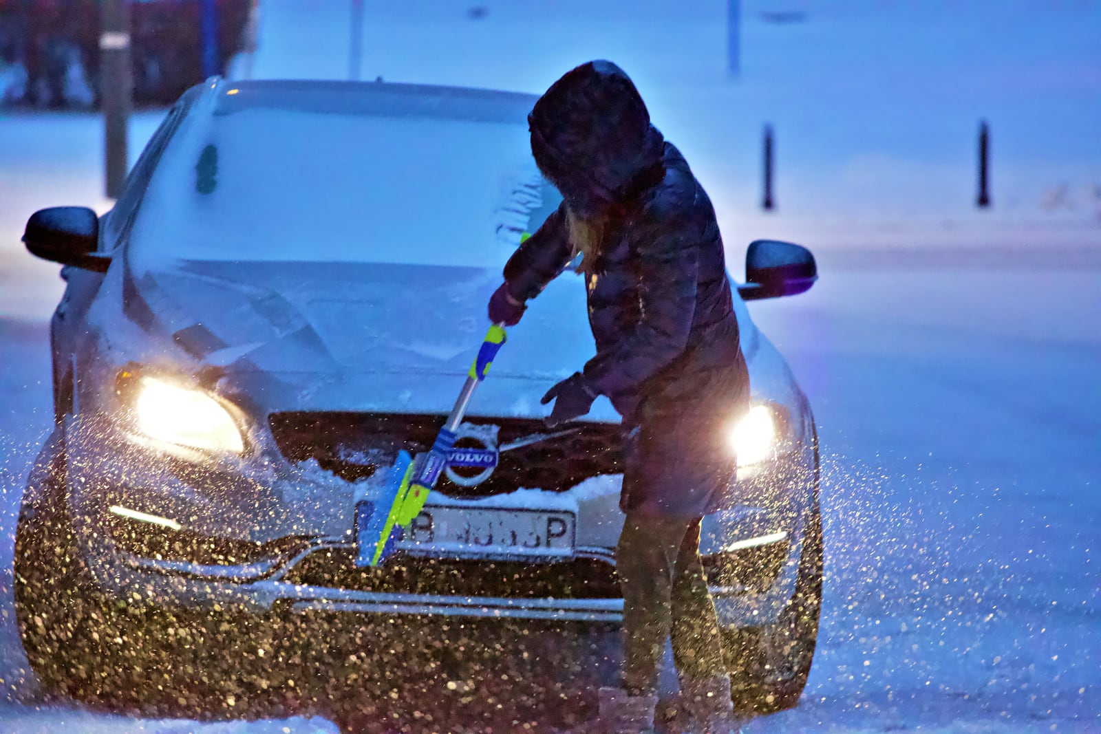 A person brushing snow from a car during snowfall